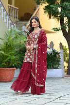 Woman in a red traditional outfit standing outdoors with plants and a staircase in the background