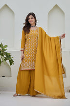 Woman wearing a mustard yellow traditional outfit with a matching dupatta in a minimalistic setting.