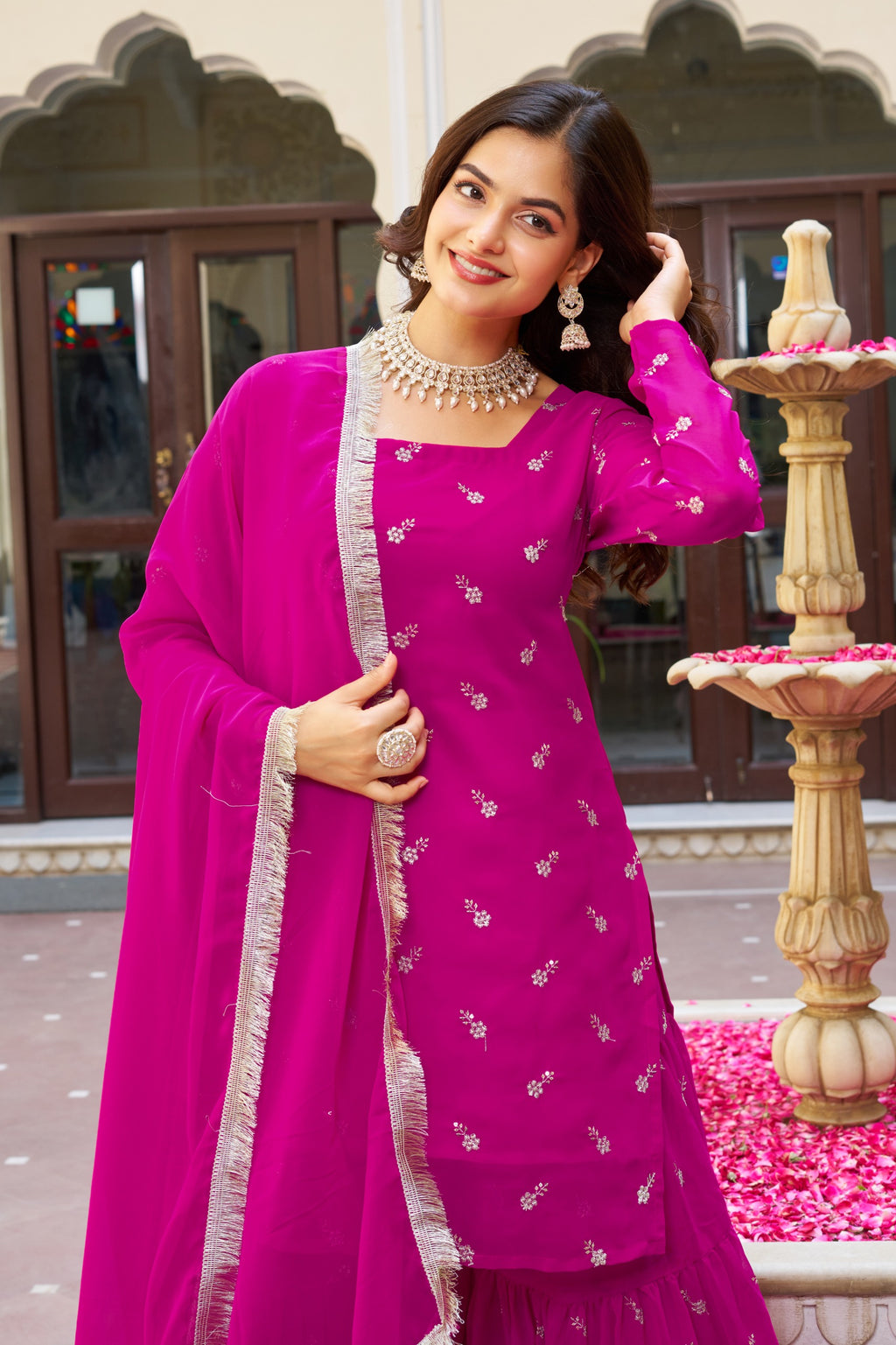 Woman in a vibrant pink traditional outfit with a matching dupatta, standing outdoors.