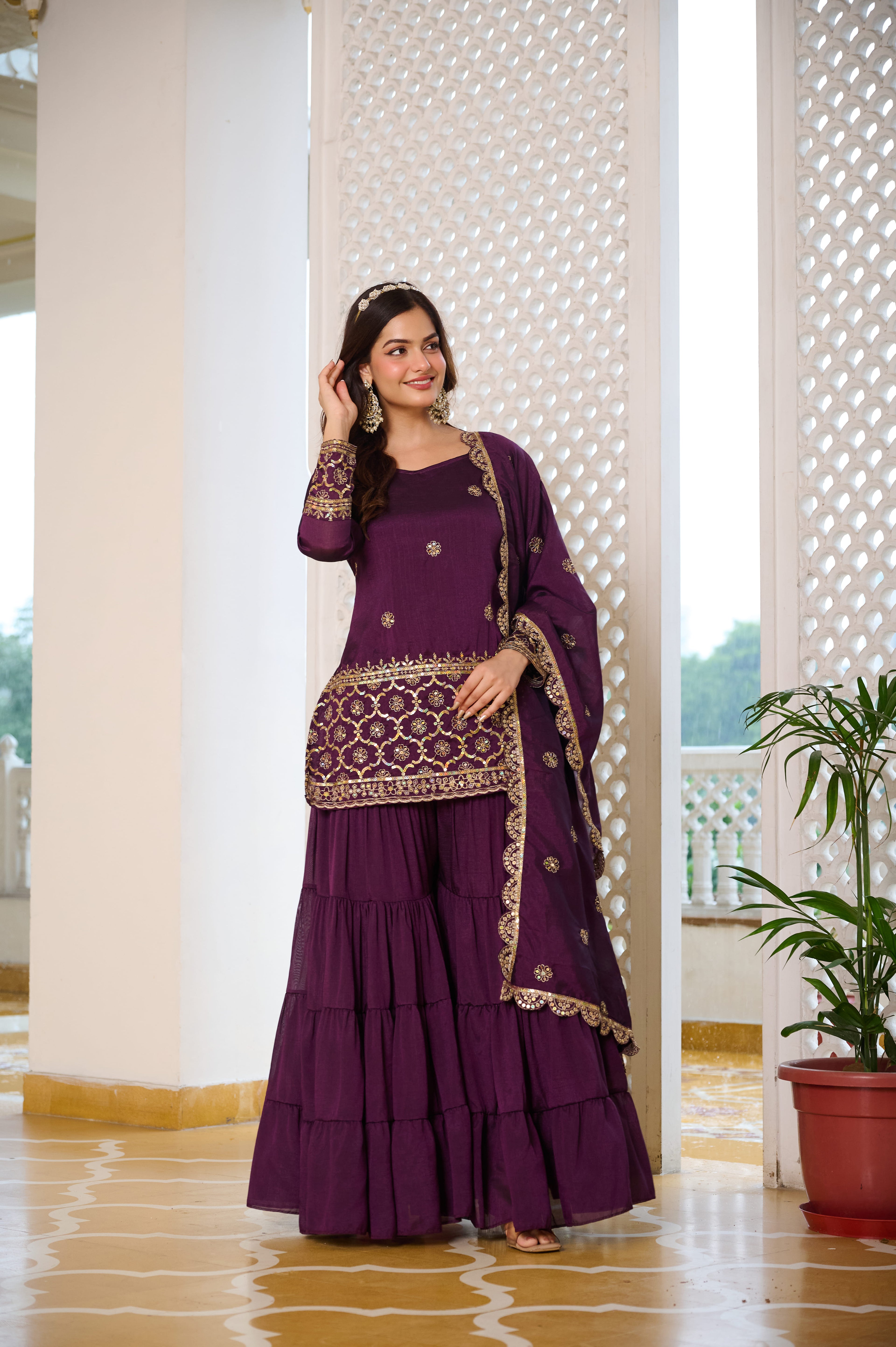 Woman in a purple traditional outfit with gold details standing indoors.