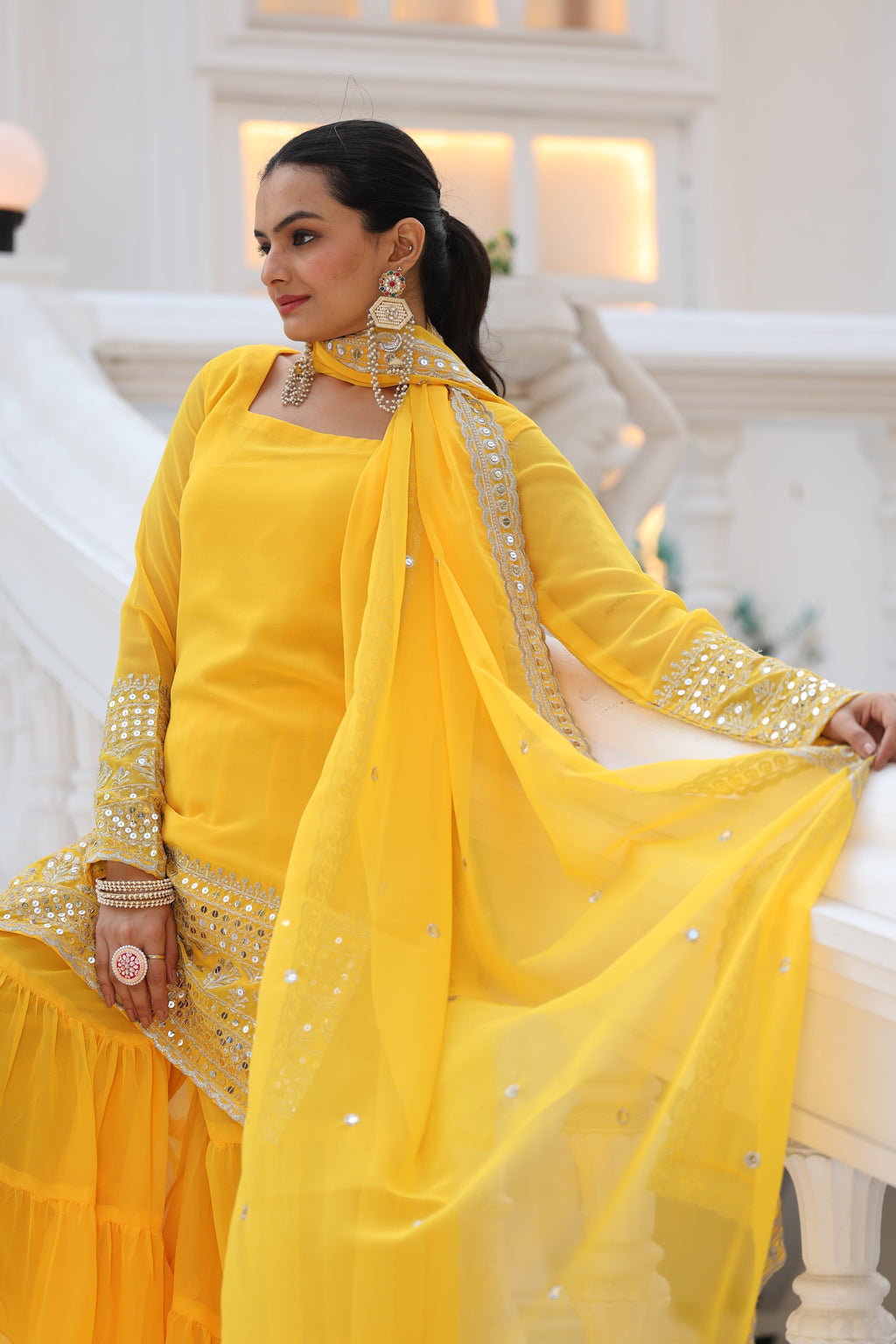 Woman wearing a yellow traditional outfit with intricate designs indoors.