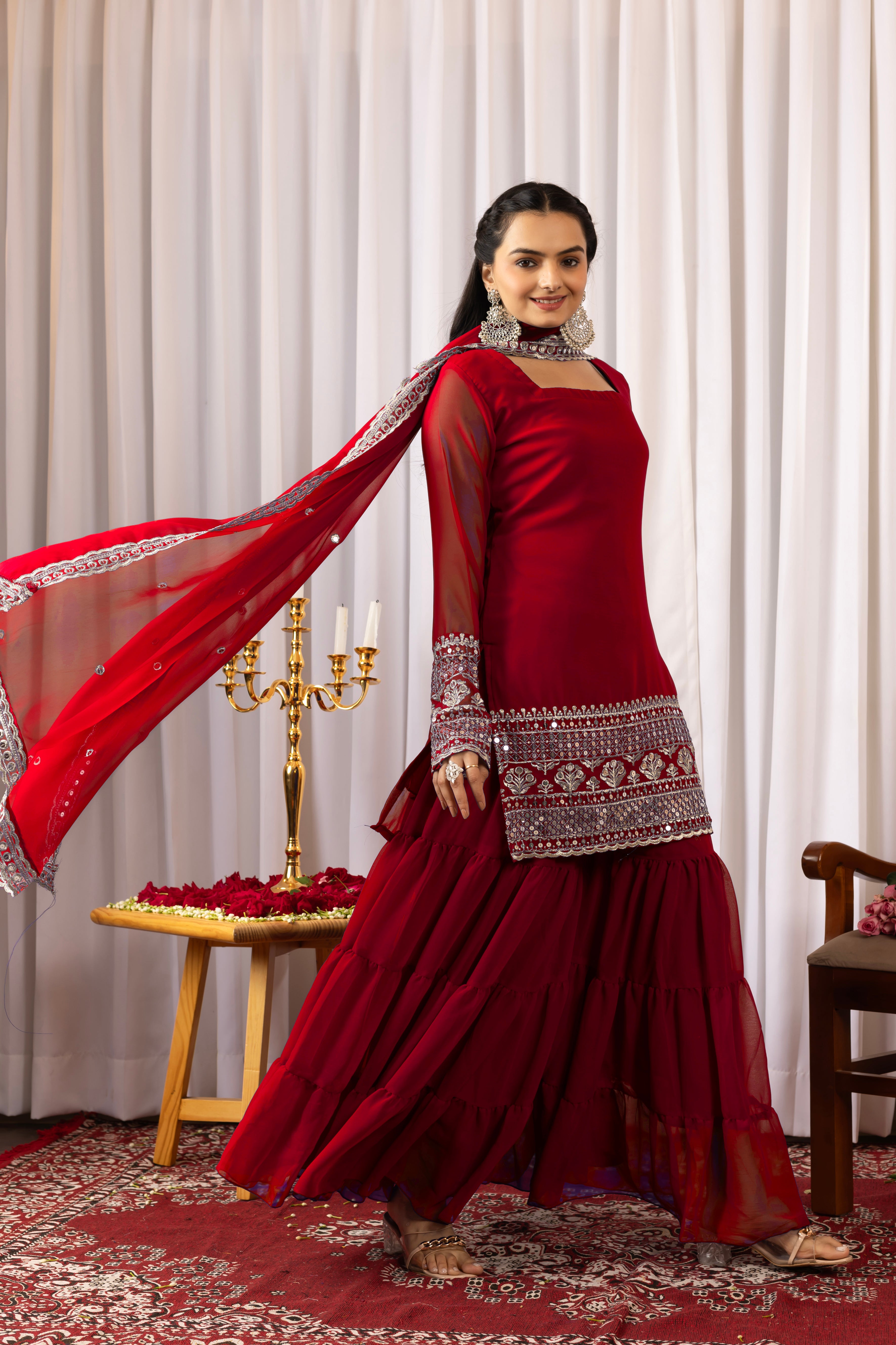 Woman in a red traditional outfit with intricate patterns against a white curtain background