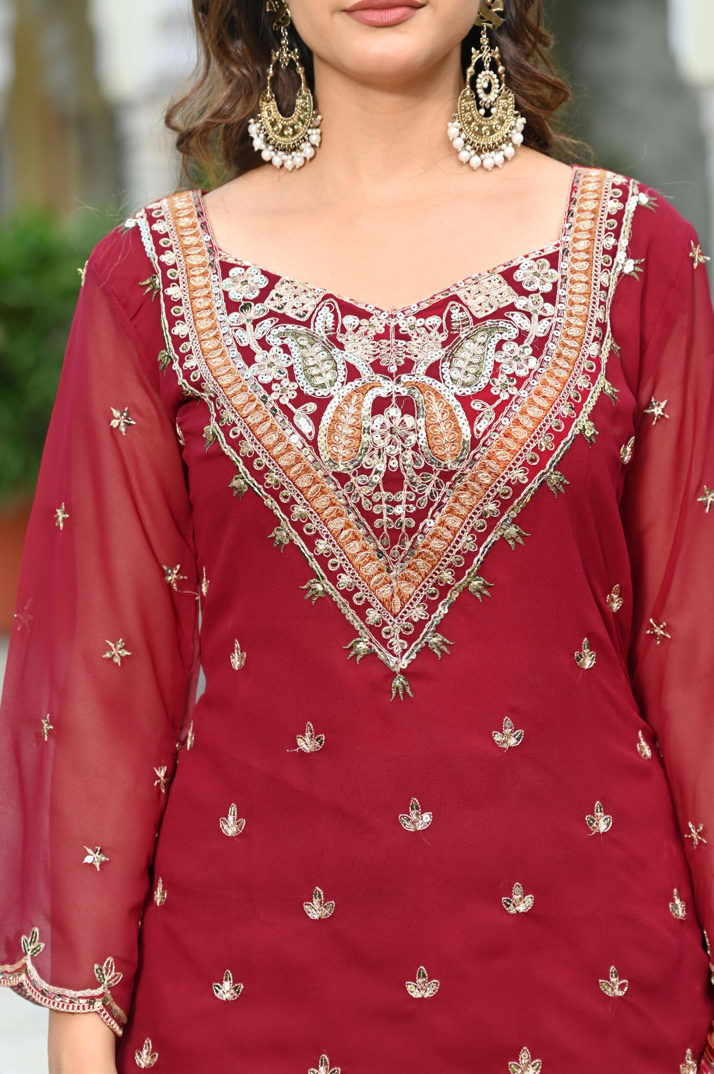 Red embroidered traditional outfit with intricate patterns and jewelry.