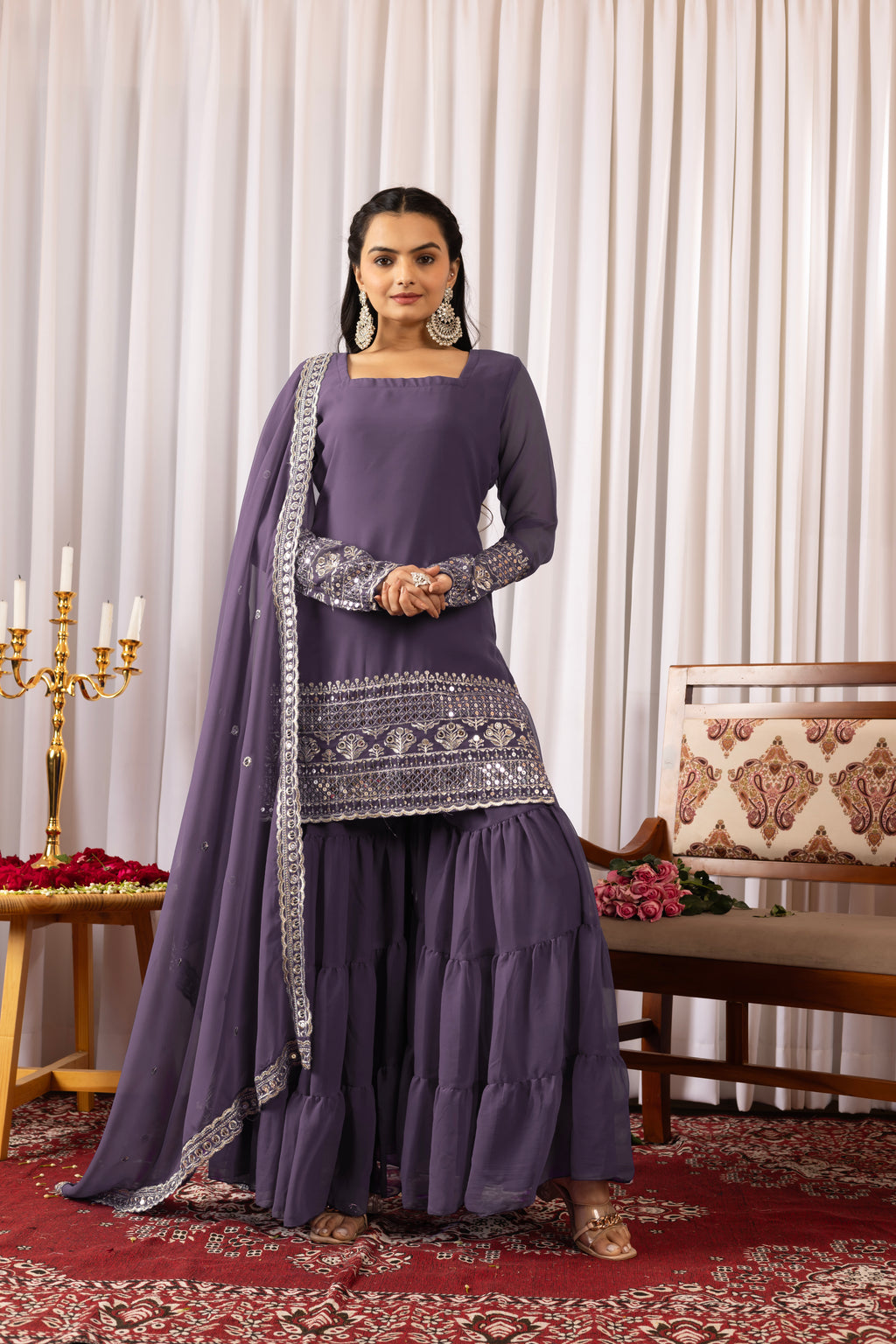 Woman in a traditional purple outfit with intricate patterns in a decorated room.
