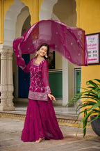 Woman in a pink traditional outfit standing in front of a yellow building with arches.