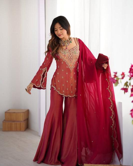 Woman in a traditional red outfit with intricate designs, holding a red dupatta.