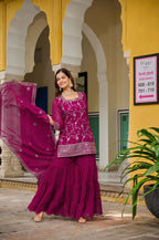 Woman in a pink traditional outfit standing in front of a yellow building with arches.