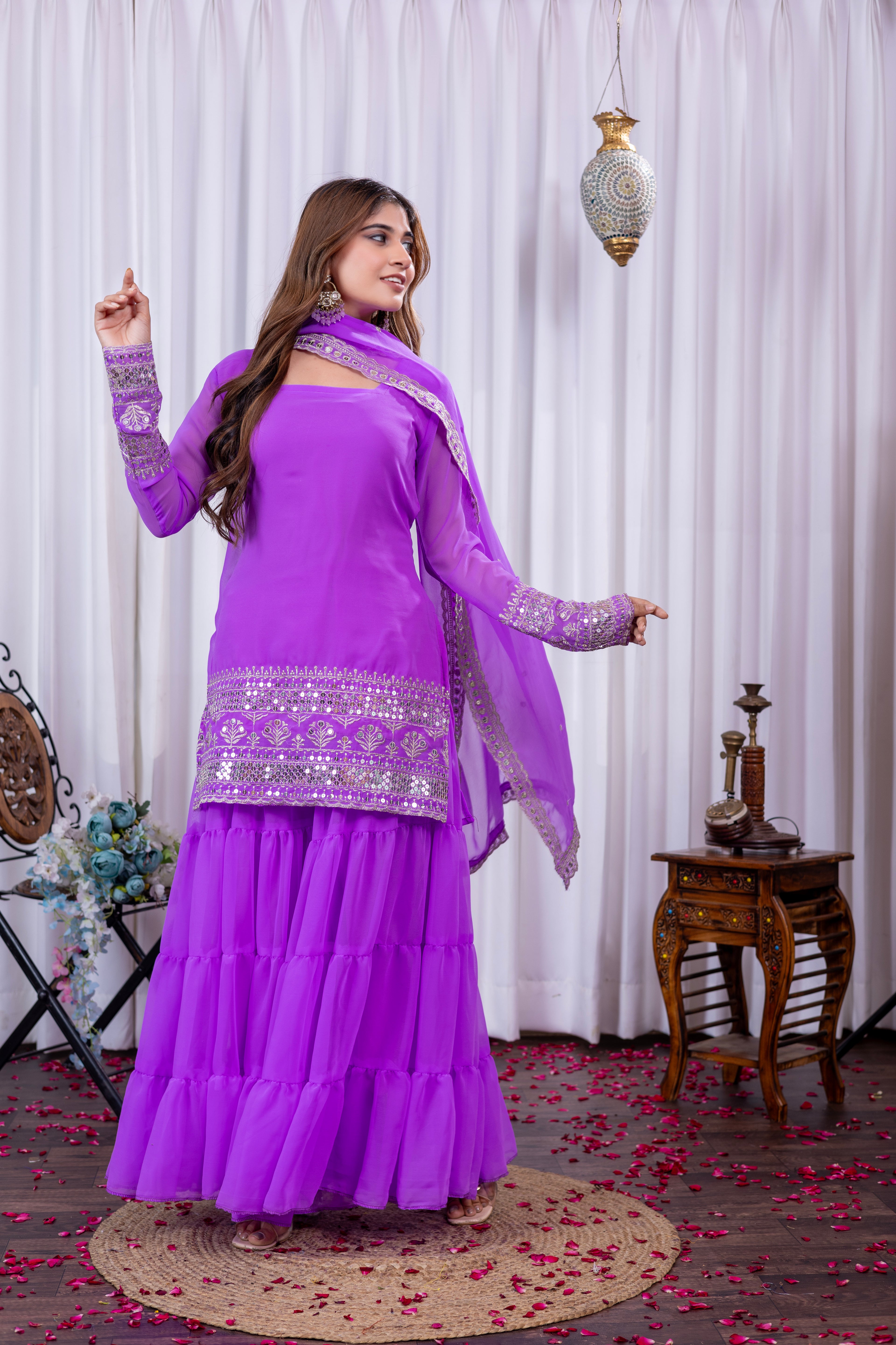 Woman in a purple traditional outfit with silver embroidery in a decorated room.