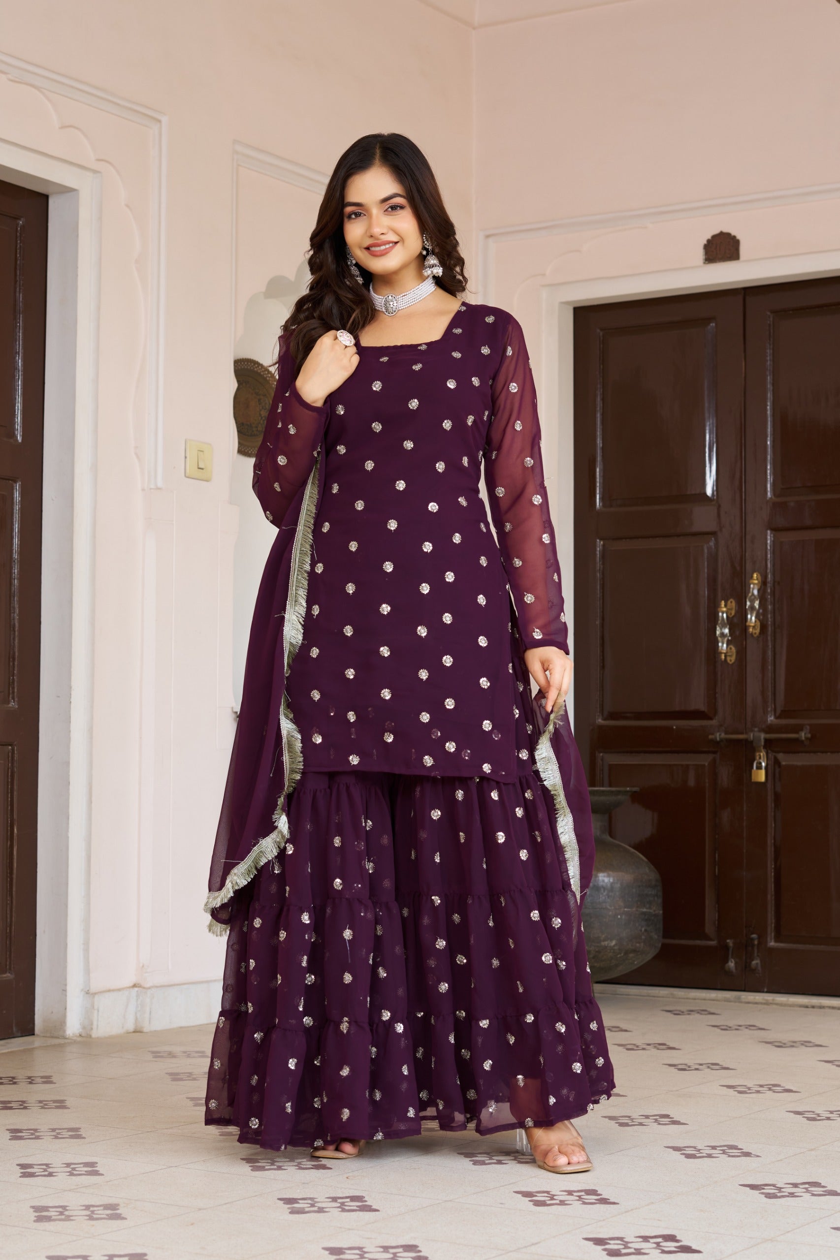 Woman wearing a purple traditional outfit with white patterns in a room.