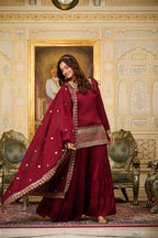 Woman in a red traditional outfit standing in an ornate room with decorative walls and furniture.
