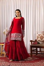 Woman in a red traditional outfit with silver embroidery standing in a decorated room.