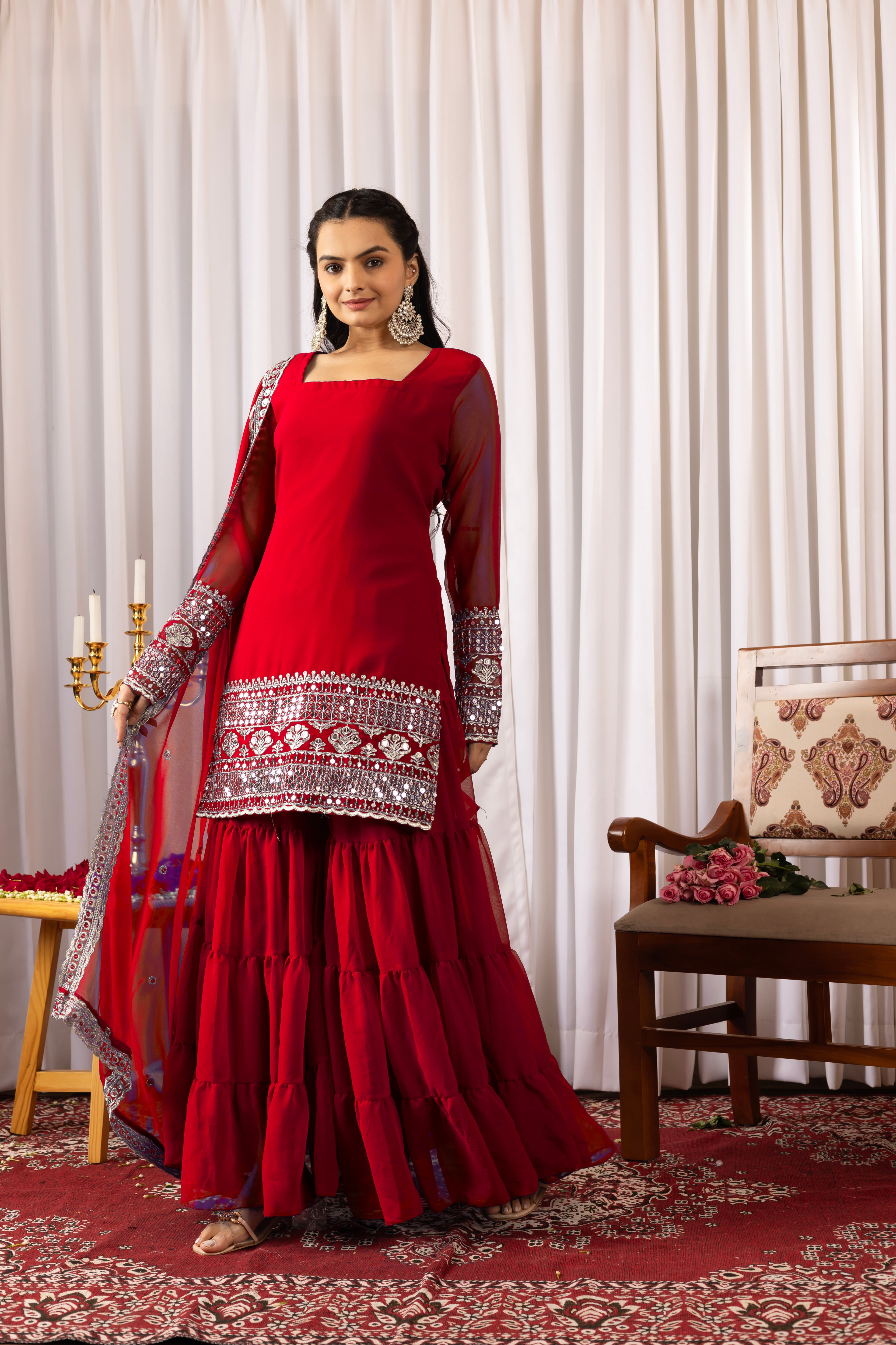 Woman in a red traditional outfit with silver embroidery standing in a decorated room.