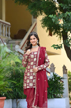 Woman in a red traditional outfit standing outdoors with greenery and a building in the background
