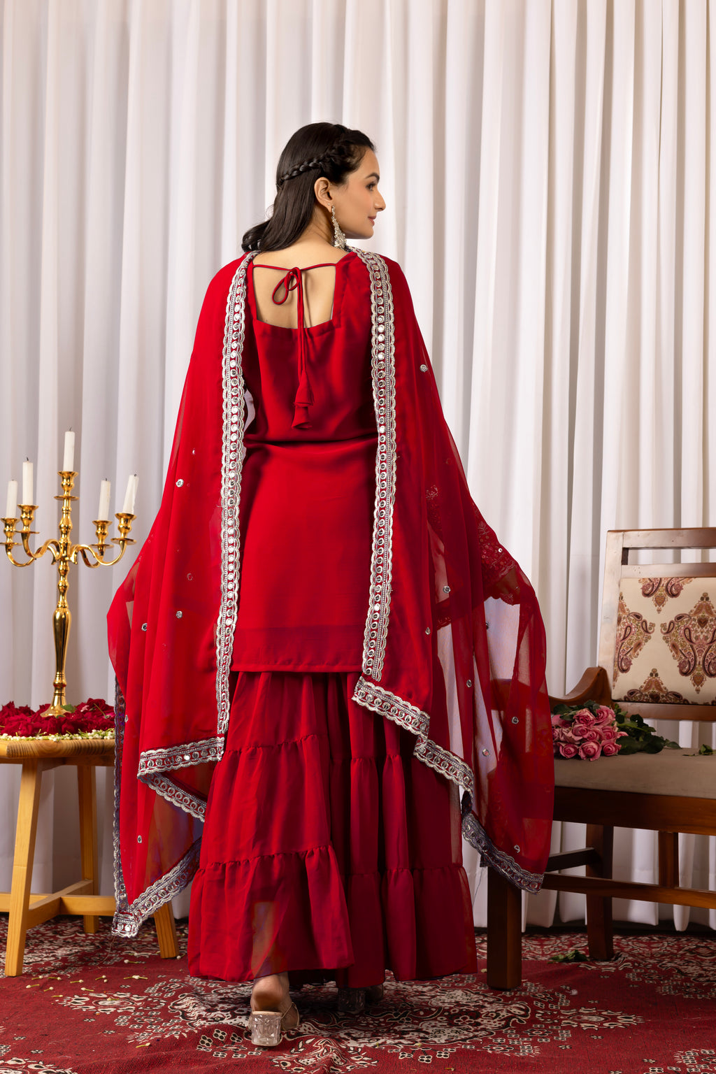 Woman in a red traditional outfit with silver details in an elegant indoor setting.