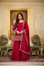 Woman in a red traditional outfit standing in an ornate room with decorative walls and furniture.