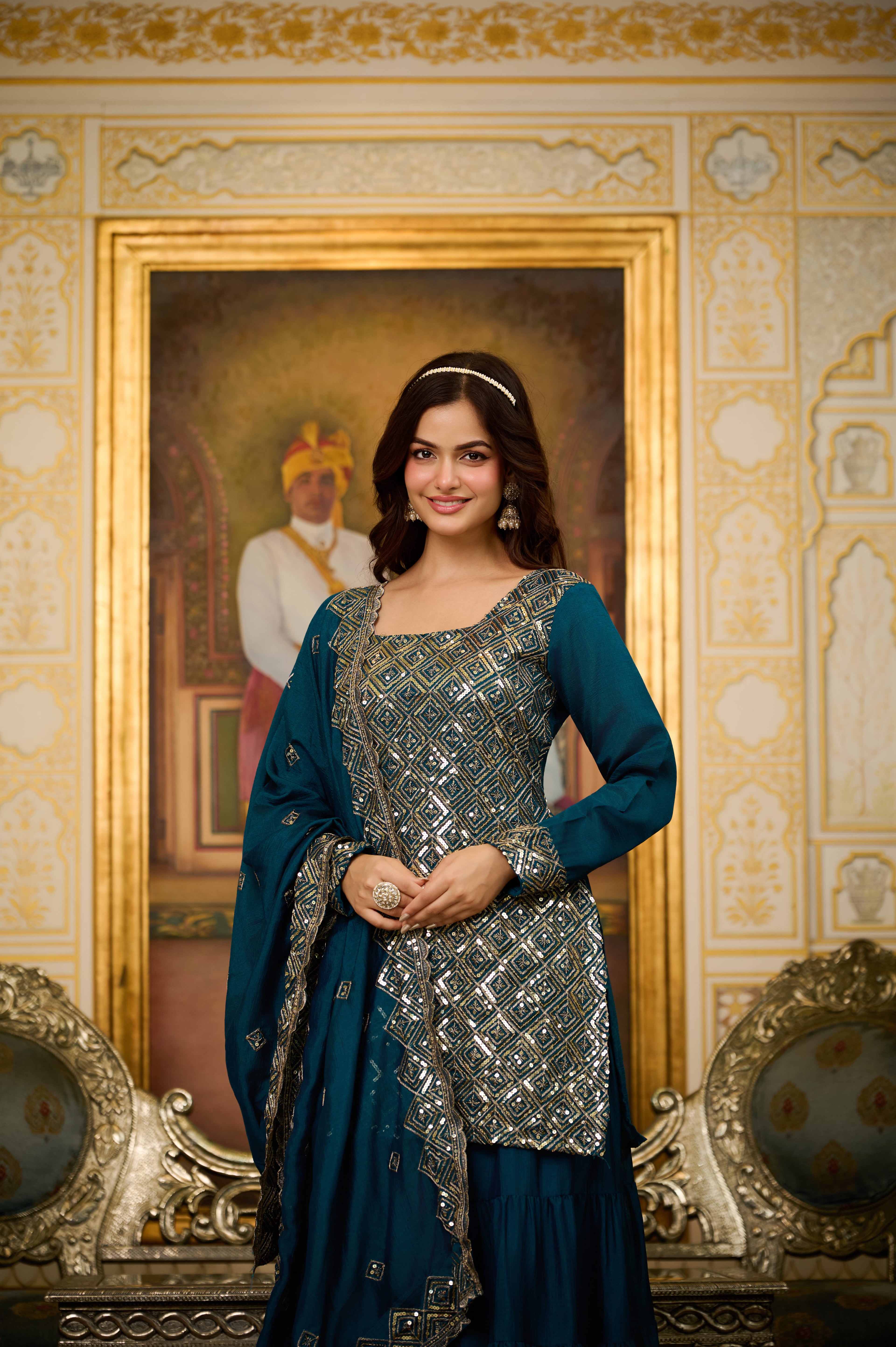 Woman in traditional attire standing in a decorated room with a portrait in the background