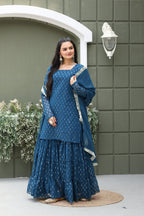 Woman wearing a blue traditional outfit standing in front of a decorative wall.