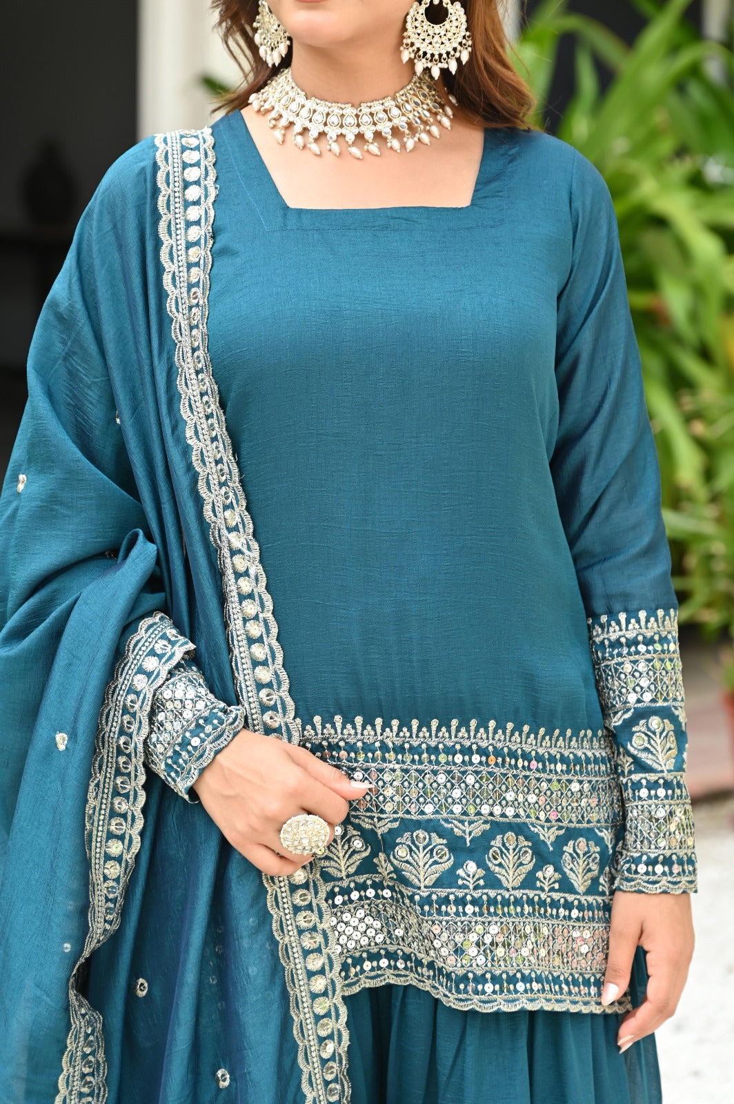 Woman wearing a teal traditional outfit with silver embroidery and jewelry.