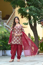 Woman in traditional maroon and gold outfit with a red dupatta outdoors.