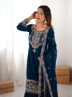 Woman wearing a dark blue embroidered traditional outfit indoors.