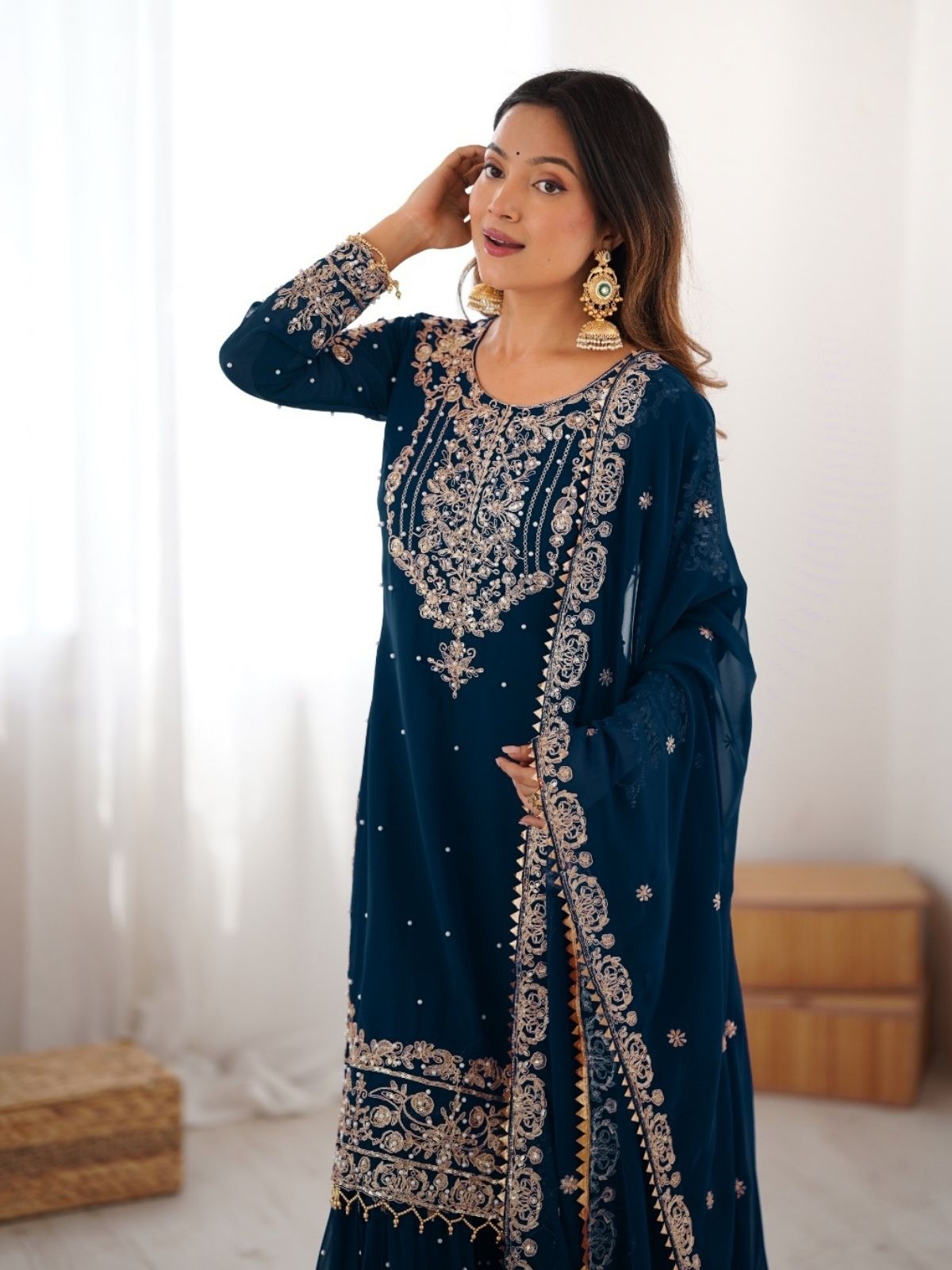 Woman wearing a dark blue embroidered traditional outfit indoors.
