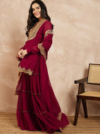 Woman wearing a maroon traditional outfit with gold embroidery against a beige background