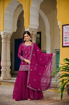 Woman in a traditional pink outfit standing in front of a yellow building with arches.