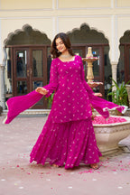 Woman in a vibrant pink traditional outfit standing in an outdoor setting with decorative elements.