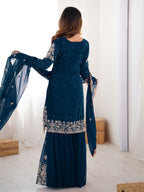 Woman wearing a dark blue embroidered traditional outfit in a minimalistic room.