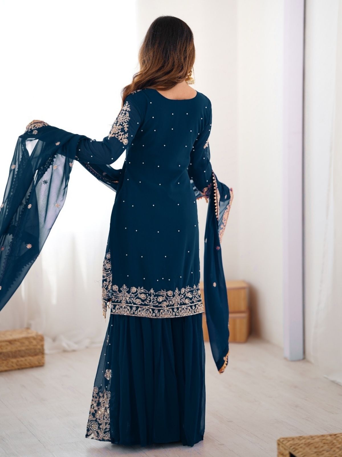 Woman wearing a dark blue embroidered traditional outfit in a minimalistic room.