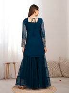 Woman wearing a dark blue traditional outfit with sheer sleeves in a minimalistic room.