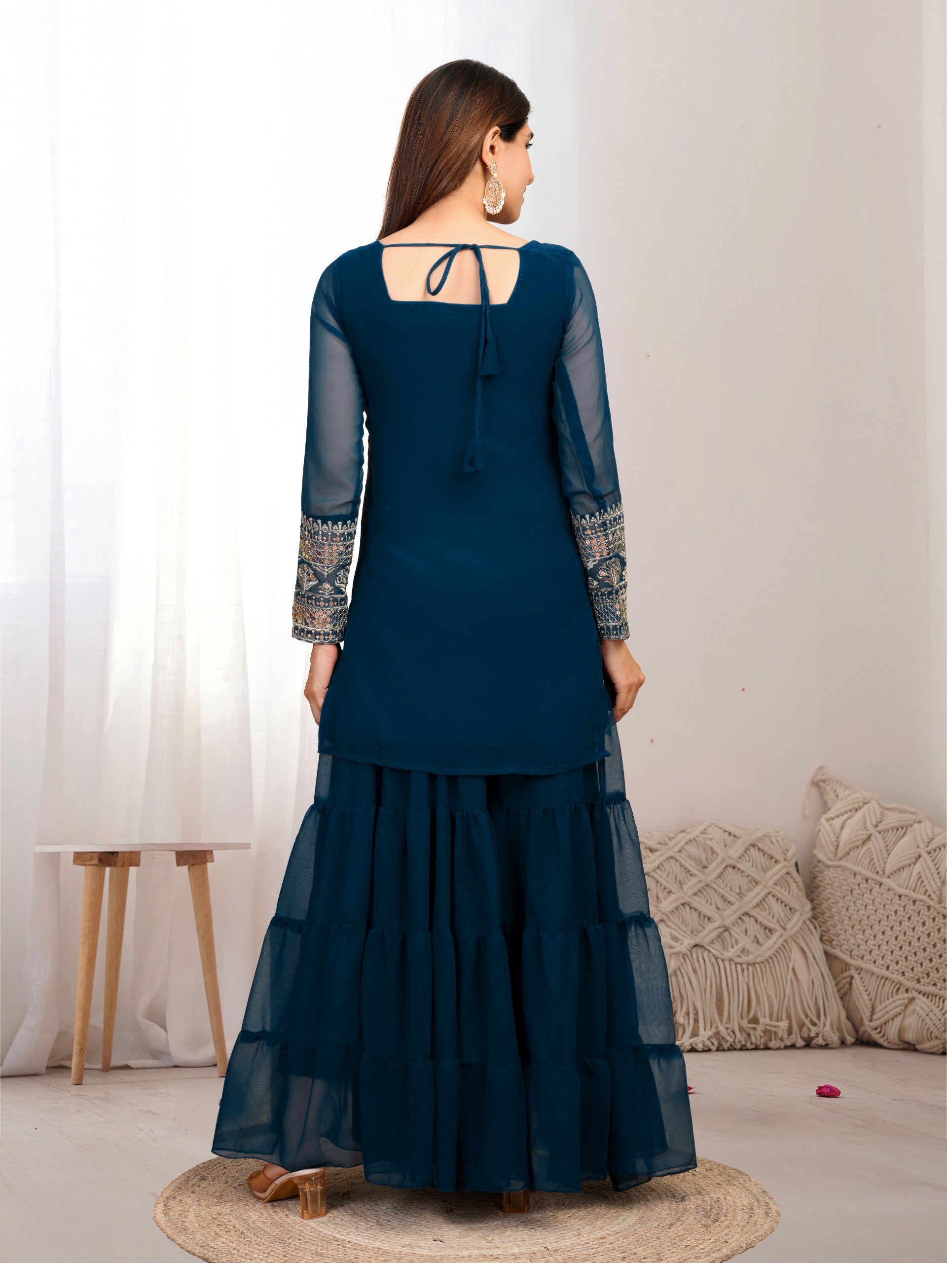 Woman wearing a dark blue traditional outfit with sheer sleeves in a minimalistic room.