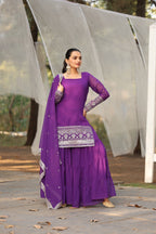 Woman wearing a purple traditional outfit with silver embroidery, standing against a neutral background.